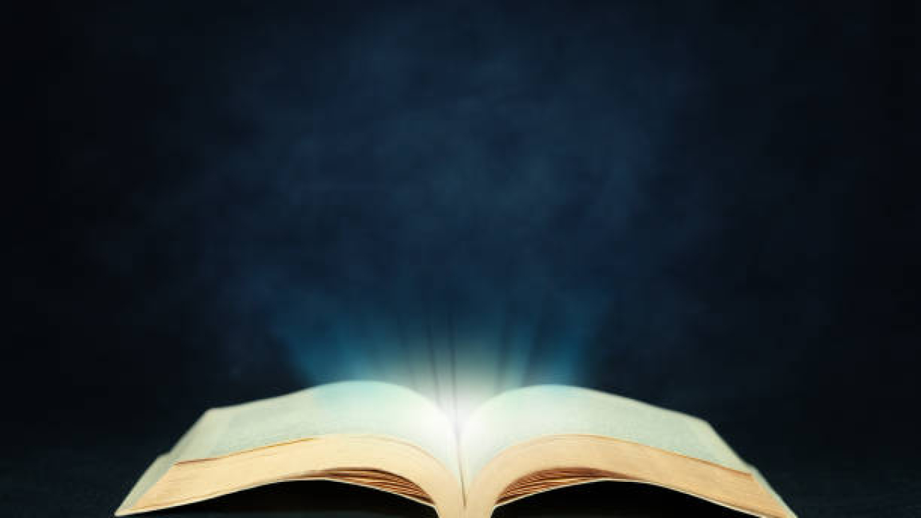 Open magic book emitting light on dark textured background and copy space