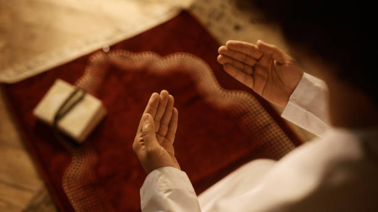 Close up of Middle Eastern man praying while sitting on traditional prayer mat at home.